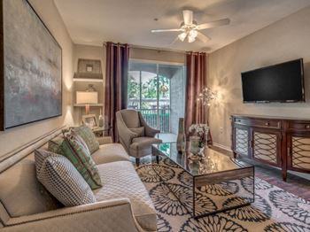 Furnished model living room area with sofa, coffee table, tv and sliding doors out to patio